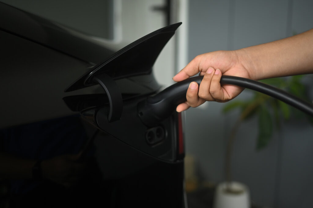 Close up of a man plugging a charging cable into a black automobile in a garage for the Maryland-home EV‑charging-guide blog.