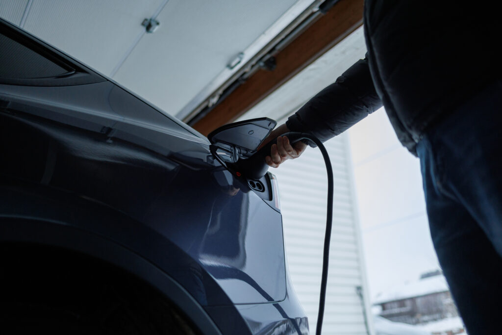 A person connects an electric vehicle to a charging station inside a clean, modern garage for best-EV-charging-routine blog.